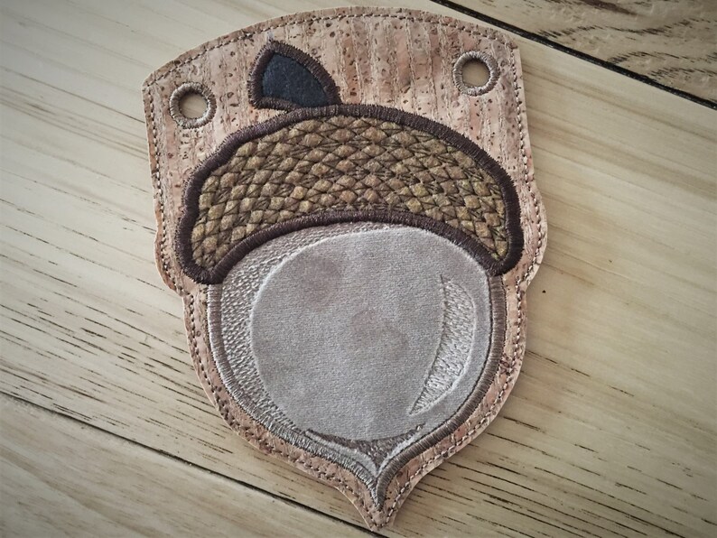 Puede incluir: Un adorno en forma de bellota de color marr&oacute;n y beige con una tapa de fieltro marr&oacute;n. El adorno est&aacute; hecho de corcho y tiene un dise&ntilde;o cosido.