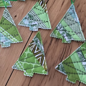 May include: A set of eight green and white patchwork fabric Christmas tree ornaments with white stitching. The ornaments are handmade and have a rustic, vintage look.