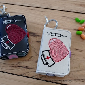 May include: Two small black and white keychains with a red heart and a syringe design. The keychains are embroidered with a nurse's cap and the text "Nurse".