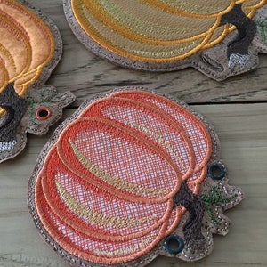 K&ouml;nnte beinhalten: Drei gestickte Stoff-Ornamente in Form von K&uuml;rbissen mit braunen Stielen und gr&uuml;nen Bl&auml;ttern. Die K&uuml;rbisse sind orange, gelb und rot mit einem strukturierten Design.