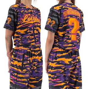 May include: A two-piece baseball-style outfit in a vibrant purple, orange, and black camouflage pattern. The top features the word "Lollita" in pink script and the number 22. The back of the shirt has a large orange question mark and the word "Sayonara".
