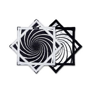 Puede incluir: Dos agarraderas cuadradas en blanco y negro con un diseño en espiral. Las agarraderas están acolchadas y tienen forma de estrella. Una tiene un borde blanco y la otra un borde negro.