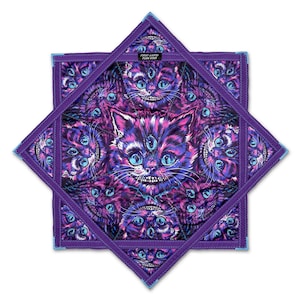May include: A star-shaped fabric mat featuring a repeating pattern of purple and blue cats with wide grins and three eyes. The center label reads FIRST EARTH FLOW STAR. The edges are finished with purple stitching and light blue trim.