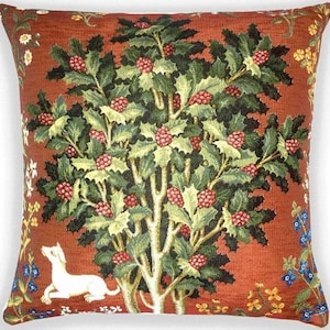 Op de afbeelding: Een kussen in tapisserie-stijl met een witte hond die voor een rode bessenstruik met groene bladeren staat. De achtergrond is rood-oranje met verschillende bloemmotieven.