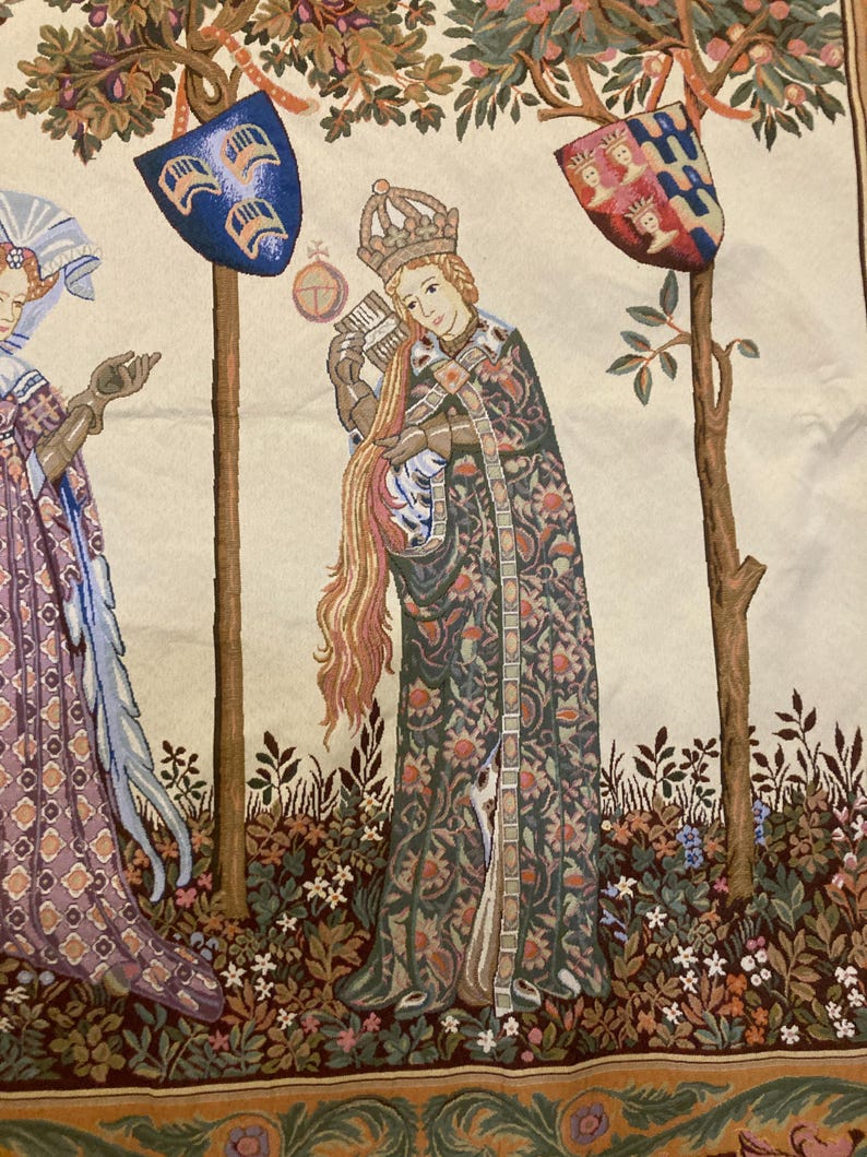 May include: A tapestry depicting a medieval scene with three figures. The central figure is a woman wearing a crown and a long, patterned robe. She is holding a book and a long, flowing strand of hair. The figures are standing in a garden setting with trees and flowers.