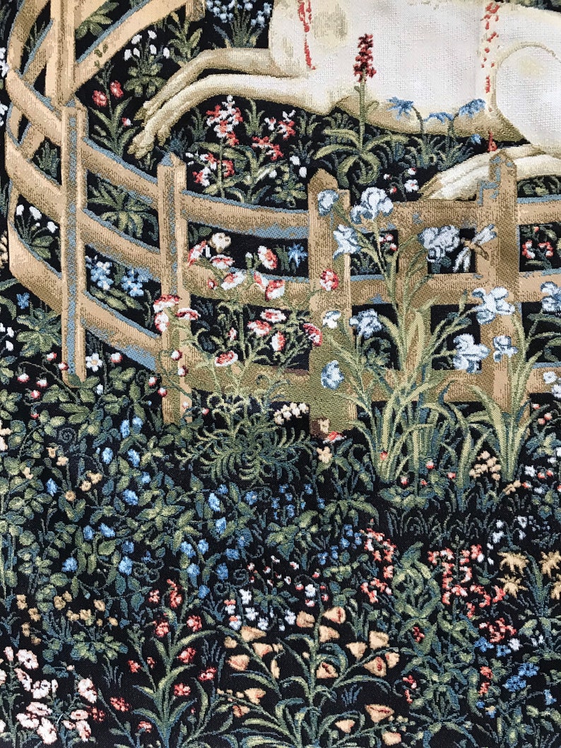 Puede incluir: Un tapiz que representa un unicornio blanco acostado en un campo de flores. El unicornio est&aacute; rodeado por una valla de madera y una variedad de flores en tonos azules, rosas, rojos y amarillos.