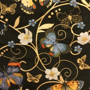 May include: Black fabric with a gold embroidered design featuring butterflies and flowers. The butterflies are in various colors, including blue, orange, and yellow. The flowers are white with gold centers.