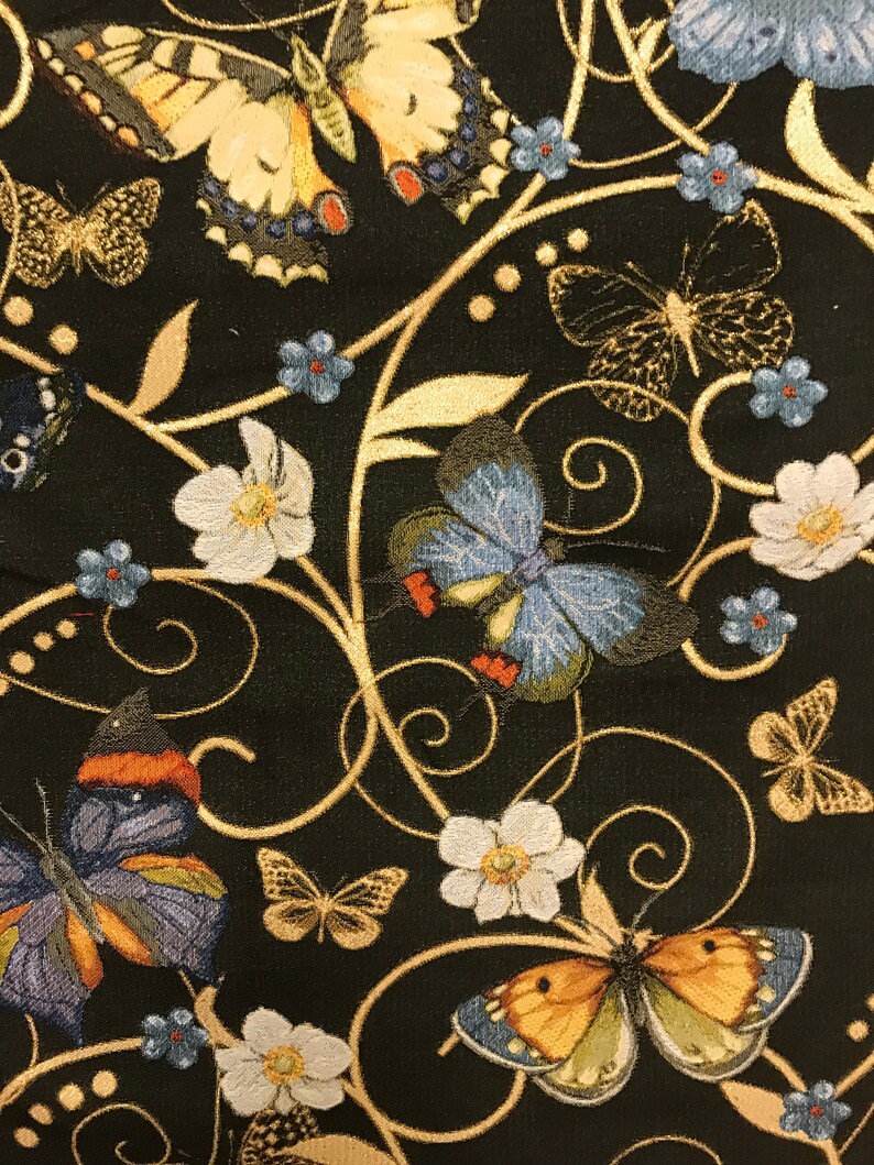 May include: Black fabric with a gold embroidered design featuring butterflies and flowers. The butterflies are in various colors, including blue, orange, and yellow. The flowers are white with gold centers.