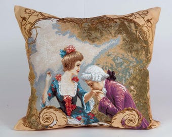 May include: A tapestry pillow featuring a couple in a garden setting. The woman is wearing a blue and white dress with a floral design. The man is wearing a purple jacket and is bowing to the woman. The background is a tapestry of green and brown colors.