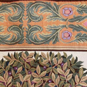 May include: Close-up of a tapestry fabric with a floral pattern. The fabric features a repeating design of green leaves, brown branches, and pink flowers. The fabric has a cream background.