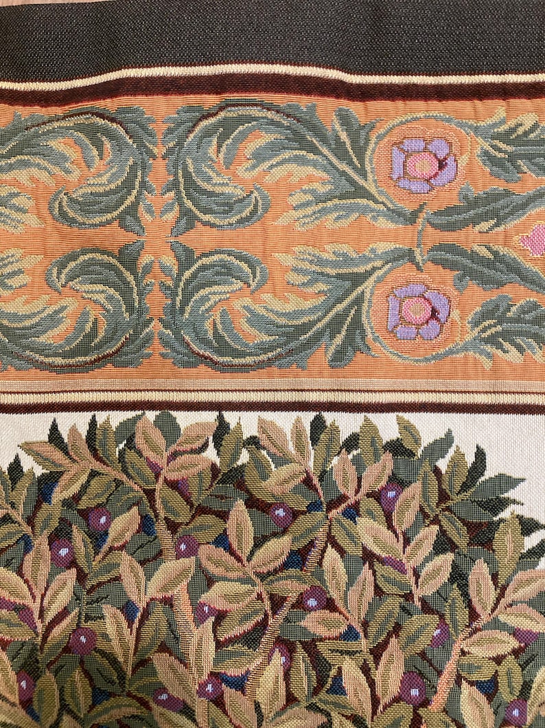 May include: Close-up of a tapestry fabric with a floral pattern. The fabric features a repeating design of green leaves, brown branches, and pink flowers. The fabric has a cream background.