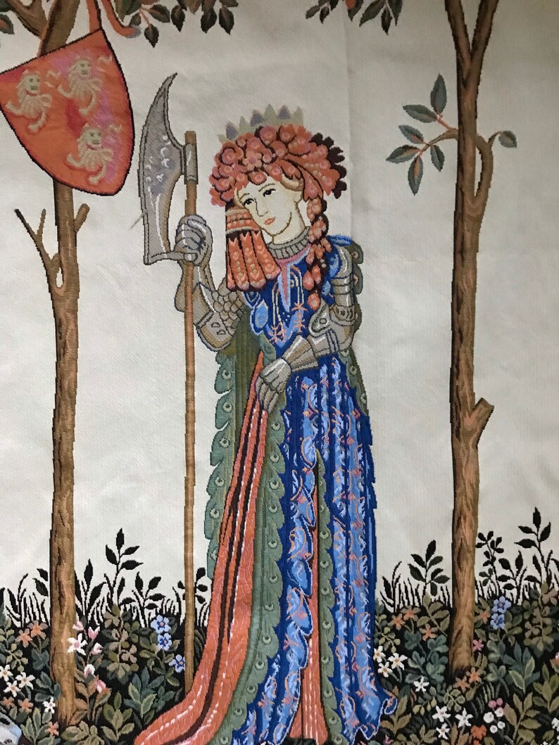 May include: A tapestry depicting a woman in armor holding a large axe. She is wearing a crown of flowers and a blue and green dress. The tapestry is set against a background of trees and flowers.