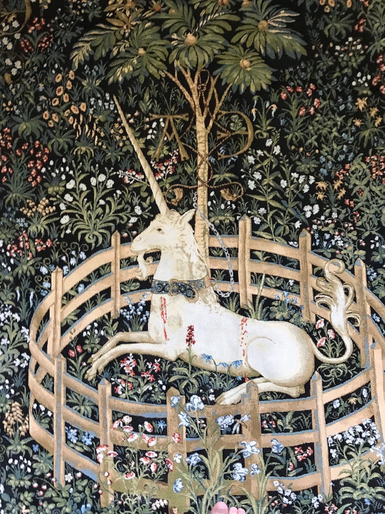 Puede incluir: Un tapiz que representa un unicornio blanco acostado en una valla circular hecha de rieles de madera. El unicornio est&aacute; rodeado de un exuberante bosque verde con flores y un &aacute;rbol en el fondo.