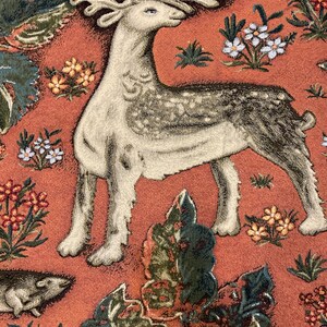 May include: A tapestry featuring a white deer with brown spots and large antlers, standing on a red background with green and orange floral designs.