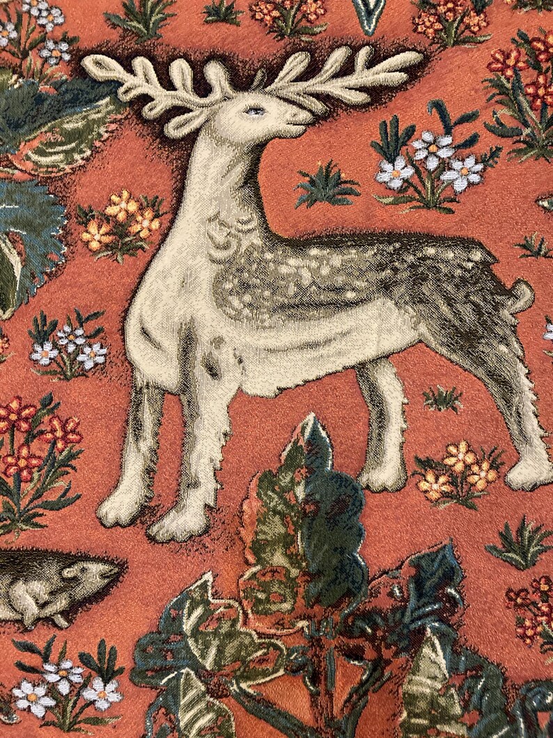May include: A tapestry featuring a white deer with brown spots and large antlers, standing on a red background with green and orange floral designs.