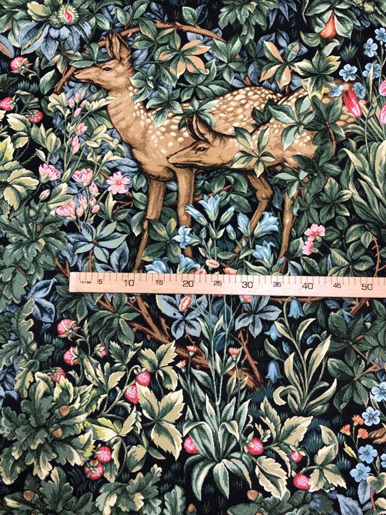 May include: A tapestry fabric featuring a dark green, brown, and blue floral pattern with two deer standing in the center. The fabric is measured with a ruler in inches.