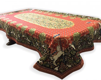 May include: Red and green tapestry tablecloth with a unicorn design. The tablecloth has a red background with a white oval in the center. The oval is filled with a green and yellow floral pattern. The unicorn is in the lower right corner of the tablecloth and is surrounded by flowers and trees.