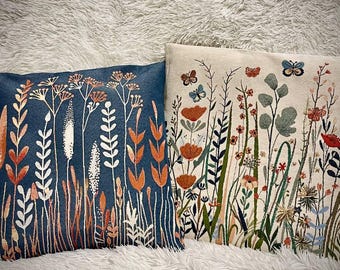 May include: Two decorative throw pillows with floral patterns. The pillow on the left has a dark blue background with white and orange floral designs. The pillow on the right has a white background with green, orange, and blue floral designs.