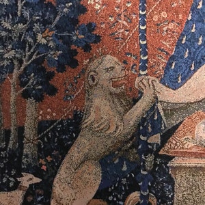 May include: A tapestry with a lion, a tree, and a woman in a blue dress. The lion is white and has a long tail. The tree is dark blue and has a brown trunk. The woman is wearing a blue dress with a white pattern. The tapestry is made of woven fabric and has a red and brown background.