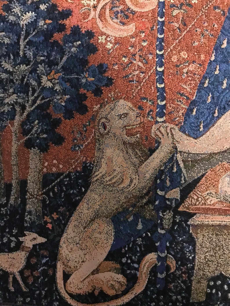 May include: A tapestry with a lion, a tree, and a woman in a blue dress. The lion is white and has a long tail. The tree is dark blue and has a brown trunk. The woman is wearing a blue dress with a white pattern. The tapestry is made of woven fabric and has a red and brown background.