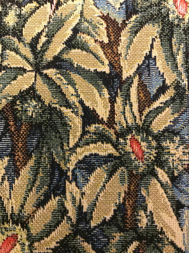 May include: Close-up of a tapestry fabric with a repeating pattern of green, brown, and blue leaves. The leaves are woven into the fabric and have a textured appearance.