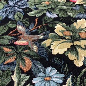 May include: A black tapestry fabric with a floral pattern featuring birds, leaves, and flowers in shades of green, blue, brown, and yellow.