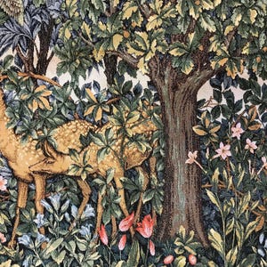 May include: Two brown deer with white spots stand in a lush green forest with pink and blue flowers. The deer are partially hidden by the foliage. A large tree trunk is visible in the background.