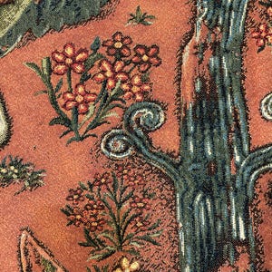 May include: Close-up of a tapestry with a detailed design of a tree with a textured bark, green leaves, and red flowers. The background is a reddish-brown color.