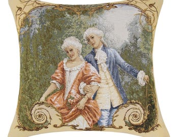 May include: A tapestry pillow featuring a couple in 18th-century clothing standing in a garden setting. The woman is wearing a red and white dress, and the man is wearing a blue coat and white shirt. The pillow has a cream background with a gold frame.