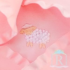 May include: A pink baby blanket with a white embroidered lamb. The blanket has a ruffled edge.