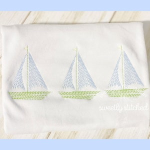May include: Three embroidered sailboats in blue and green on a white fabric background. The sailboats are stitched with small dots.