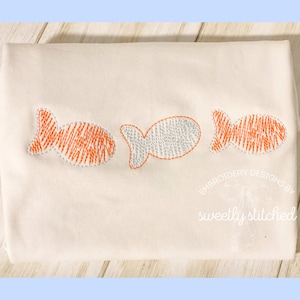 May include: Three embroidered fish designs on a white fabric. The fish are in a row, with the middle fish in gray and the two outer fish in orange.