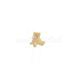 May include: A small, yellow teddy bear with a pink bow sits on a white background. The bear has a sweet expression and is holding a pink bow in its paws.