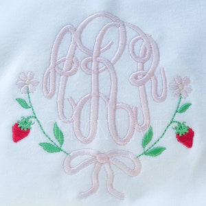 May include: Pink embroidered monogram with a bow and two strawberries and flowers on either side.