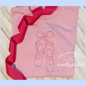 May include: A pink t-shirt with a red ribbon and an embroidered design of two ballet shoes tied together with a bow.