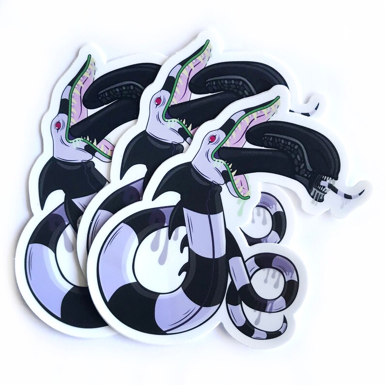 May include: Three black and white striped stickers with a purple and green creature with a large mouth and sharp teeth. The creature is depicted with a black and white striped body and a green tongue.