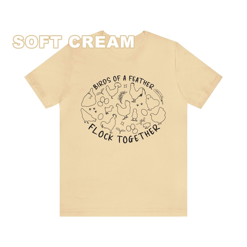 K&ouml;nnte beinhalten: Ein T-Shirt in zartem Cremeton mit einer schwarzen Grafik von H&uuml;hnern und Eiern in einem Kreis mit dem Text "Birds of a feather flock together".