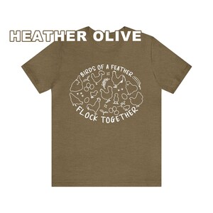 K&ouml;nnte beinhalten: Ein T-Shirt in der Farbe Oliv-Melange mit einer wei&szlig;en Grafik von H&uuml;hnern und Eiern. Die Grafik lautet "Birds of a Feather Flock Together".