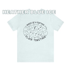 K&ouml;nnte beinhalten: Ein hellblaues T-Shirt mit einer schwarz-wei&szlig;en Illustration von H&uuml;hnern und Eiern. Der Text "Birds of a Feather Flock Together" ist auf dem T-Shirt aufgedruckt.