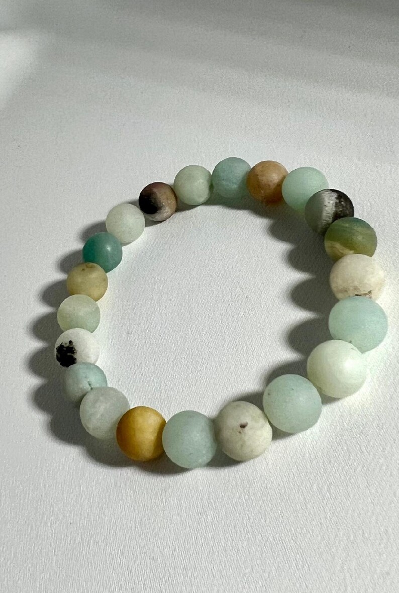 Puede incluir: Un brazalete hecho de cuentas verdes, azules y marrones. Las cuentas son redondas y tienen un acabado liso y pulido.