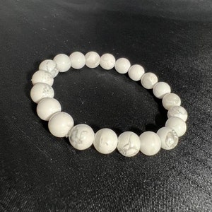 May include: White beaded bracelet with a marbled pattern. The bracelet is made of round, polished beads strung together. The beads have a smooth texture and a subtle, natural variation in color.