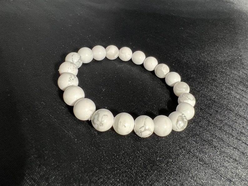 May include: White beaded bracelet with a marbled pattern. The bracelet is made of round, polished beads strung together. The beads have a smooth texture and a subtle, natural variation in color.