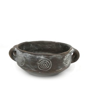 Peut inclure: Un bol en céramique brune avec deux anses et un motif géométrique blanc. Le bol est en terre cuite et a un aspect rustique.