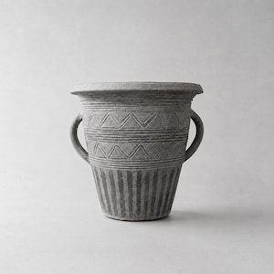 Può includere: Un vaso in ceramica grigia e strutturata con due manici. Il vaso presenta un motivo dettagliato di linee orizzontali e triangoli. La metà inferiore presenta linee verticali. Il vaso ha un bordo ampio e svasato.