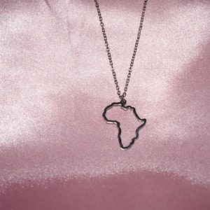 May include: A silver chain necklace with an outline of the continent of Africa as the pendant. The necklace is displayed on a pink satin background.