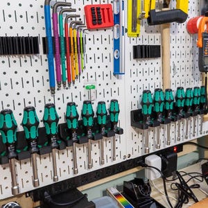 May include: A collection of tools organized on a white pegboard. The tools include screwdrivers with green and black handles, various Allen wrenches, a hammer, and other hand tools. The tools are neatly arranged for easy access.