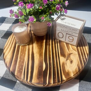 K&ouml;nnte beinhalten: Ein dreistufiges Tablett aus Holz mit einer dunkelbraunen Beize. Das Tablett ist mit einer kleinen Topfpflanze mit lila Bl&uuml;ten, einer wei&szlig;en Kerze und einem Holzblockkalender verziert, der "Dienstag, Mittwoch, M&auml;rz 09" anzeigt.