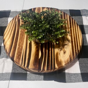 K&ouml;nnte beinhalten: Ein rundes Holztablett mit einem dunkelbraunen Holzmaserungsmuster. Das Tablett hat eine nat&uuml;rliche Holzoptik und ist mit einer kleinen gr&uuml;nen Pflanze in der Mitte verziert.