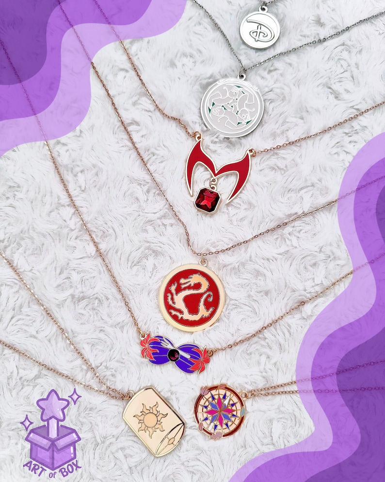 May include: A set of seven gold-tone necklaces with various charms, including a dragon, a compass, a sun, a crown, a magic wand, and a flower. The necklaces are displayed on a white fluffy surface.