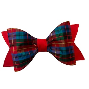 May include: A large, decorative bow with a vibrant plaid pattern in red, green, blue, and gold. The bow has a solid red backing and center, creating a striking contrast. This accessory is suitable for various occasions.